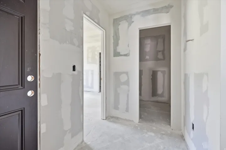 Interior hallway featuring unfinished drywall, a dark paneled door, and exposed electrical outlets