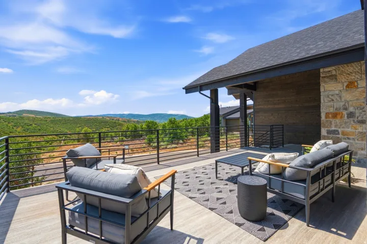 Spacious outdoor patio featuring a sloped asphalt shingle roof, stone veneer wall, horizontal metal railing, and wood-finish flooring