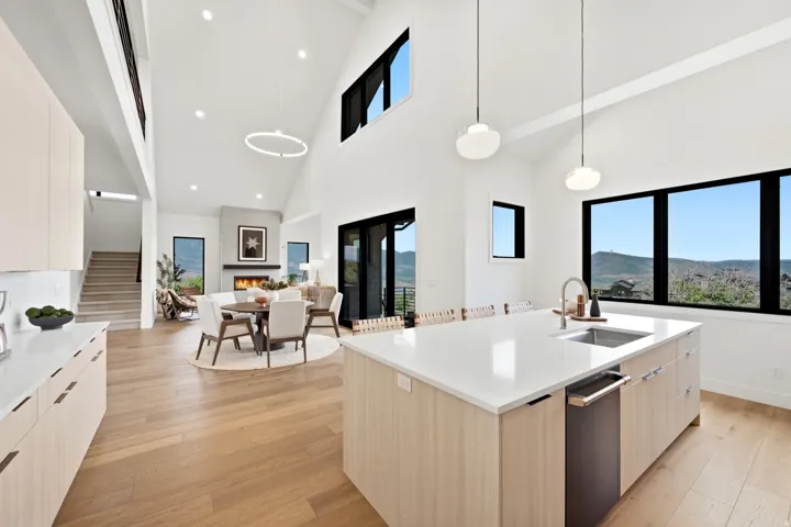 Open-concept living space with vaulted ceilings, wood-finish flooring, a contemporary fireplace, and an expansive kitchen island featuring a built-in sink and dishwasher