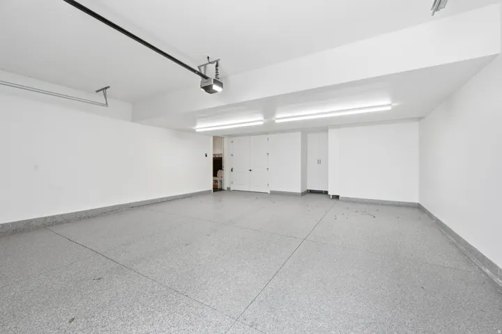 Spacious garage featuring epoxy-coated flooring, white finished walls, ample overhead lighting, and built-in storage cabinetry