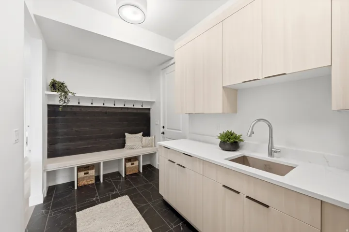 Mudroom with built-in bench seating and hooks, dark wood-finish accent wall, and black tile flooring