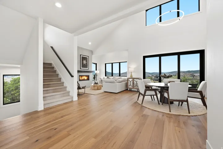 Open-concept living space featuring wood-finish flooring, a contemporary fireplace with a stone-look surround, and ample natural light from large windows