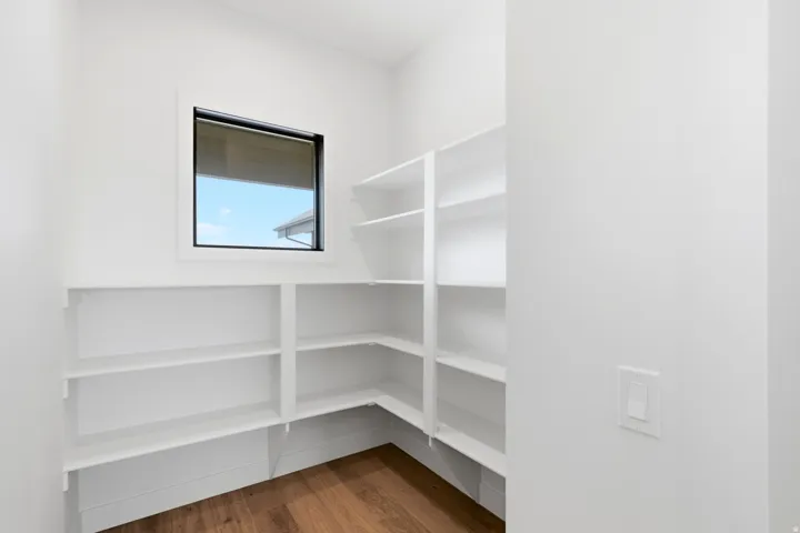 Spacious pantry featuring extensive built-in shelving, a natural wood-finish floor, and a window with a roller shade