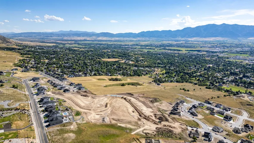 Expansive aerial perspective showcasing a developing residential area with modern homes, surrounded by natural landscapes and distant mountains