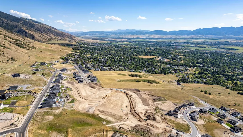 Aerial perspective showcasing a developing residential area with established homes and ongoing construction, framed by a mountainous landscape and distant cityscape