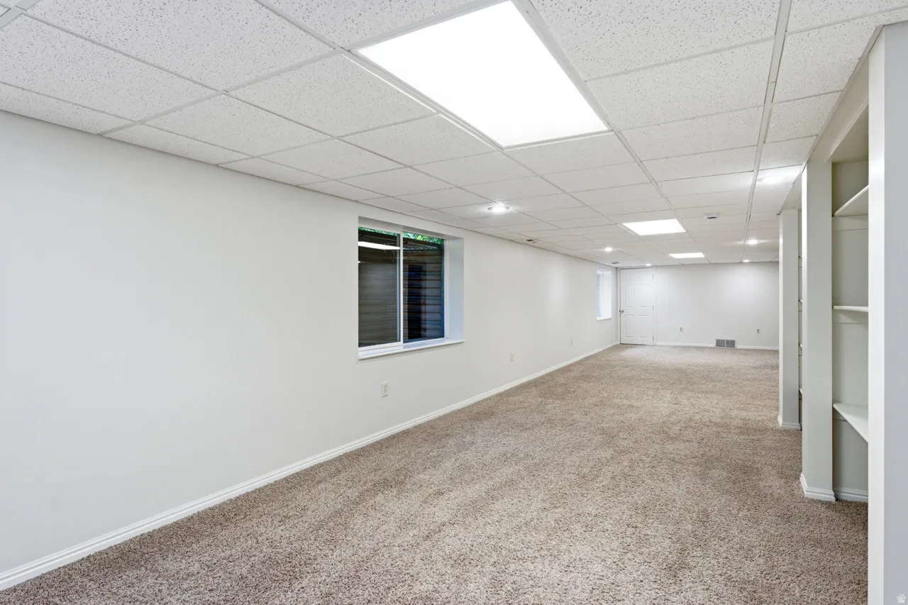 Spacious finished basement featuring recessed lighting, drop ceiling, light brown carpet, a horizontal window, and built-in shelving