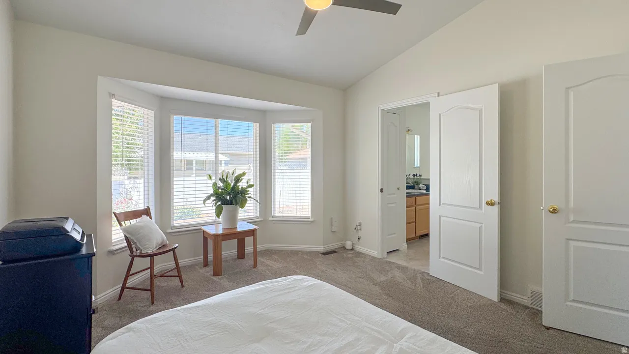 Vaulted ceiling bedroom featuring a bay window, carpet flooring, a ceiling fan, and a white paneled door