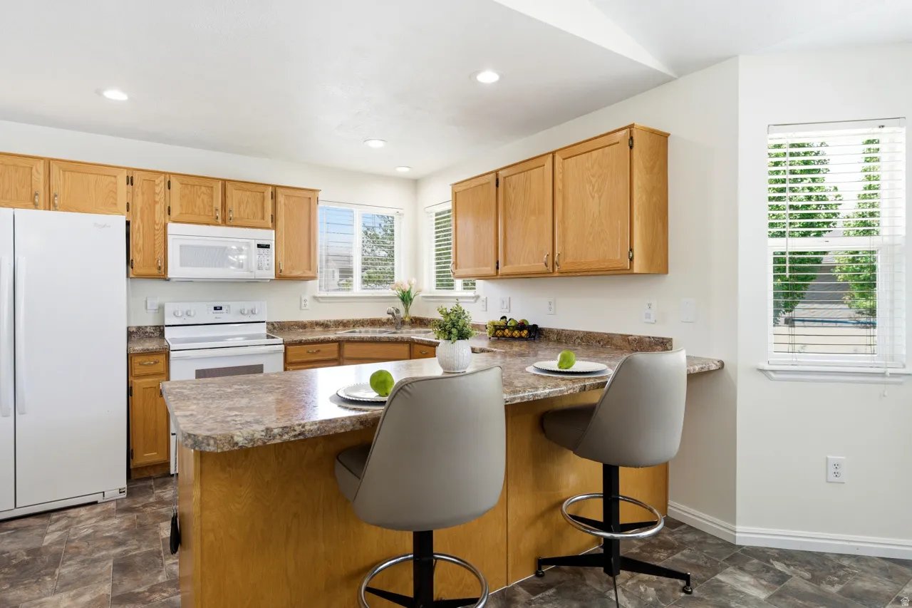 Kitchen featuring wood cabinetry, white appliances, a breakfast bar with seating, and L-shaped counters