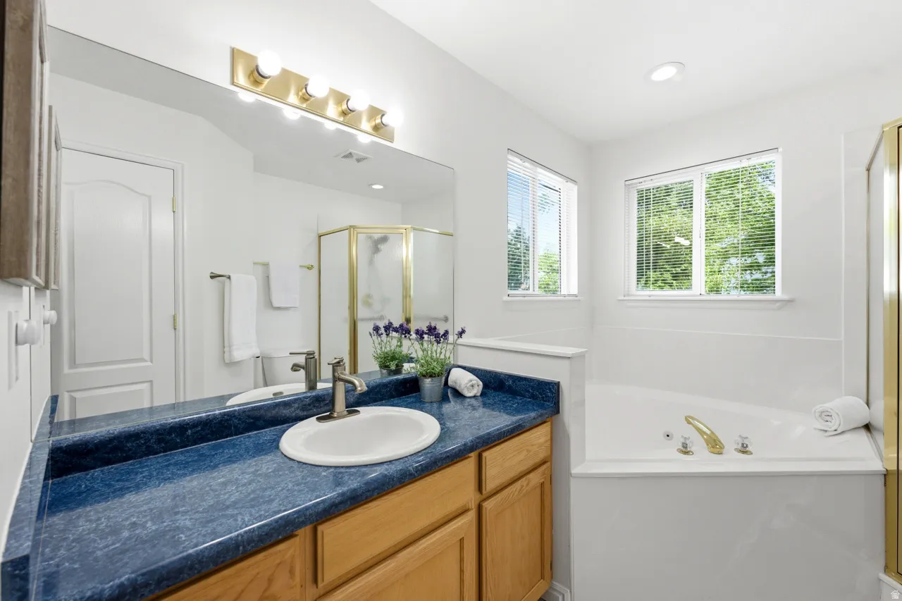 Bathroom featuring a soaking tub, dual windows with blinds, a shower enclosure, and a vanity with an integrated sink and wood-finish cabinetry