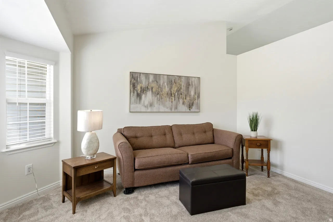 Bright interior space featuring light neutral wall paint, a window with horizontal blinds, textured carpeting, and a sloped ceiling