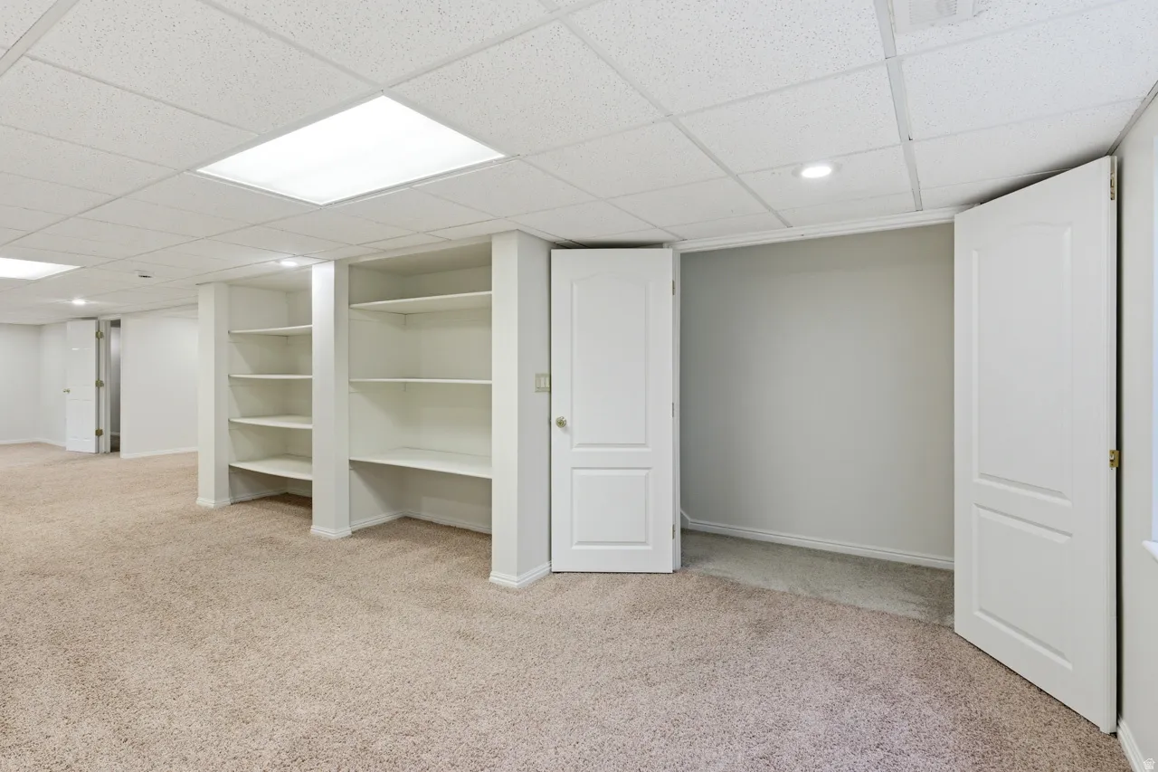 Spacious room featuring neutral carpeting, built-in shelving, two interior doors, recessed lighting, and a drop ceiling with integrated lighting panels