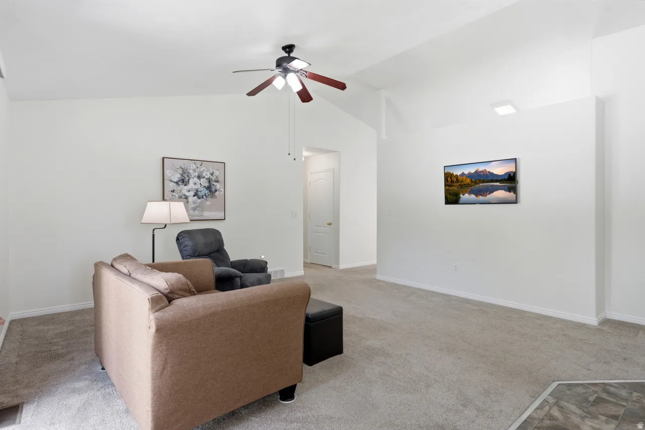Expansive living area featuring vaulted ceilings, light-colored carpeting, a ceiling fan with integrated lighting, and a wall-mounted flat-screen television
