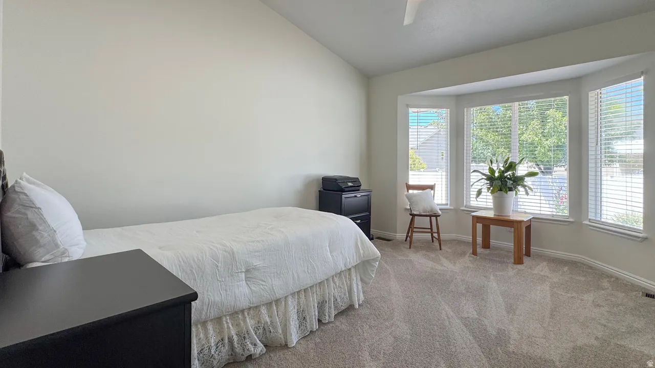 Spacious room featuring vaulted ceilings, bay windows with blinds, and soft grey carpet