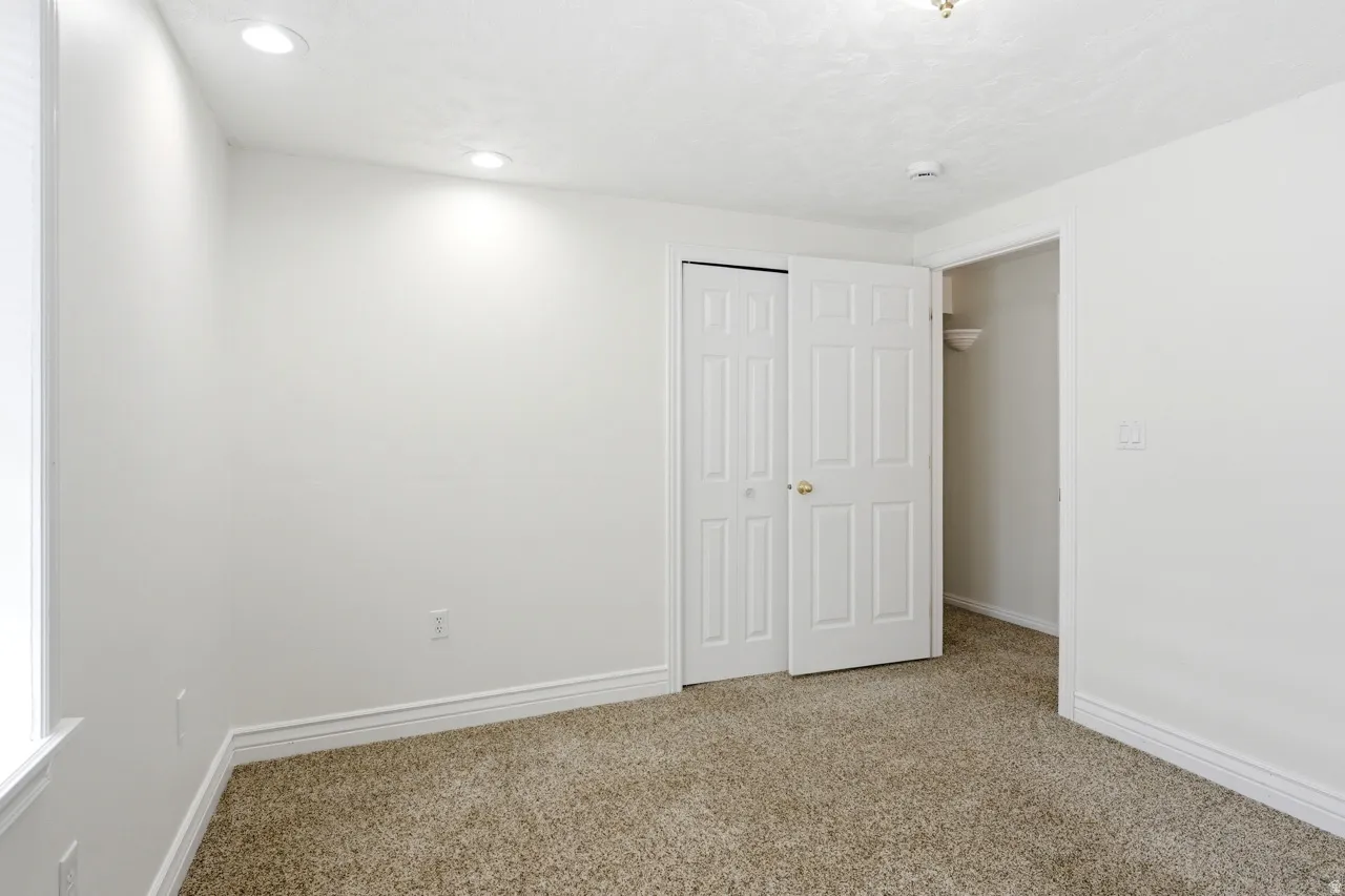 Carpeted room featuring white walls, white trim, recessed lighting, and a closet with bifold doors