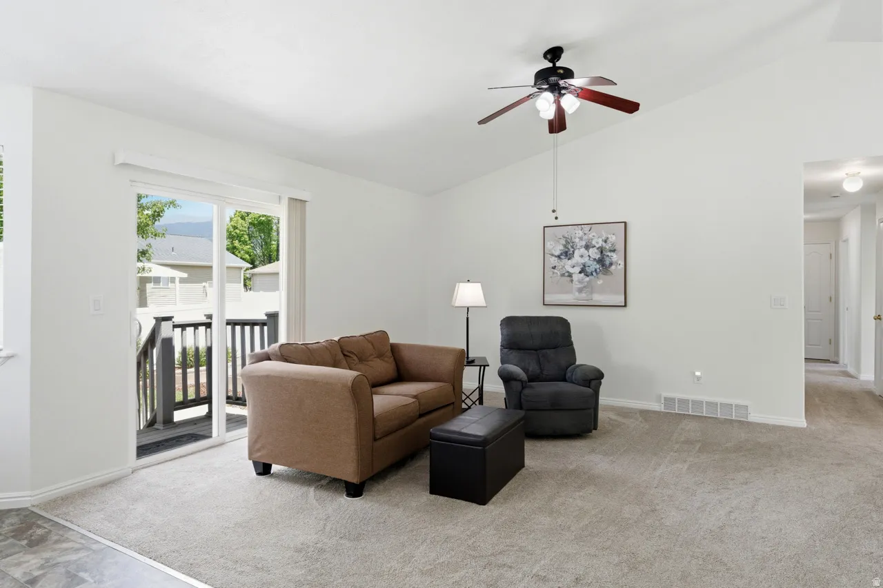 Spacious living area featuring vaulted ceilings, light-toned carpeting, and a ceiling fan with integrated lighting