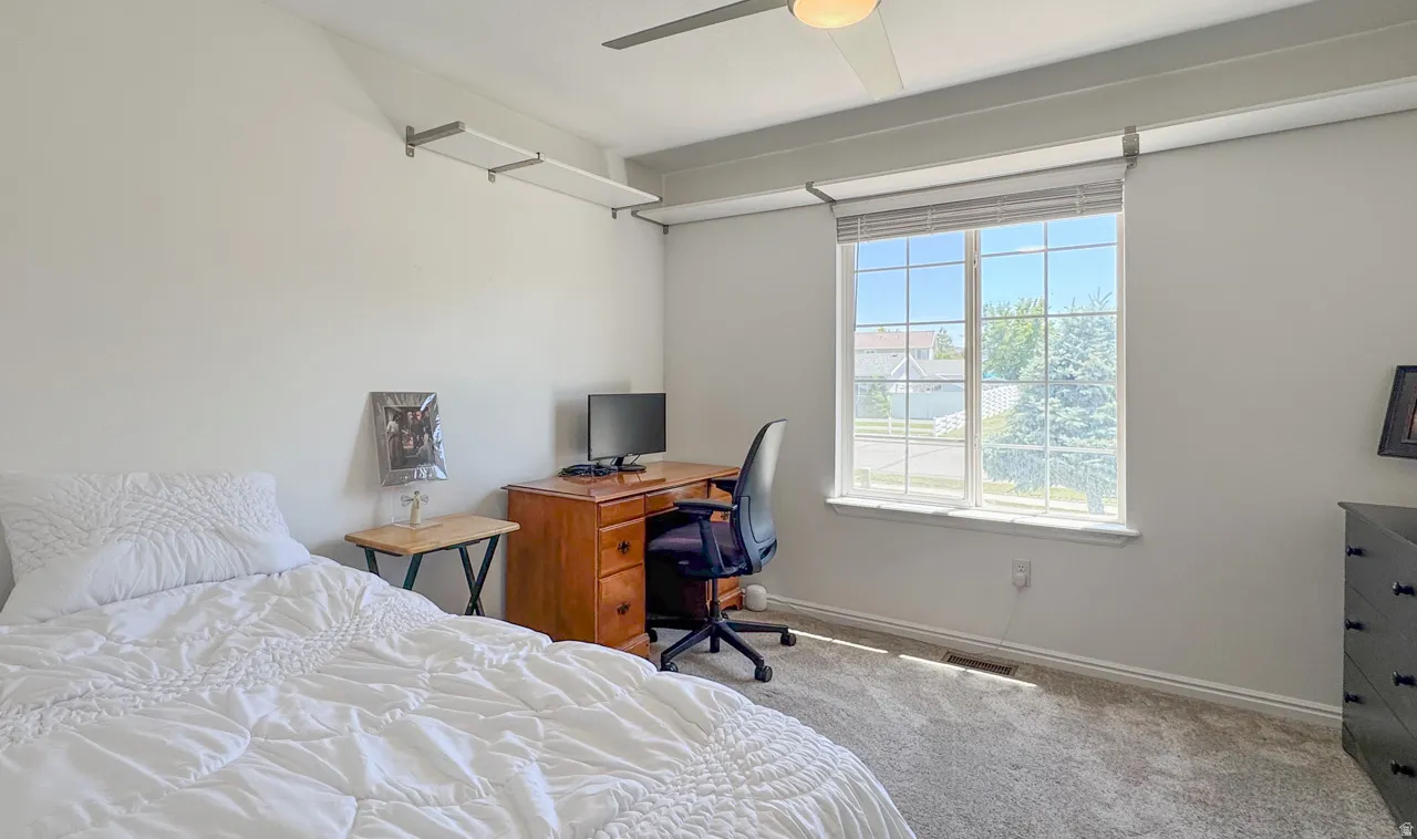 Carpeted room featuring a large window, ceiling fan, and built-in wall shelving
