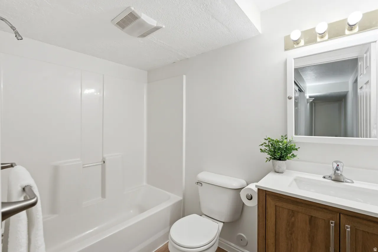 Bathroom featuring a white bathtub with shower, toilet, and a vanity with a wood-finish cabinet, white countertop, and integrated sink