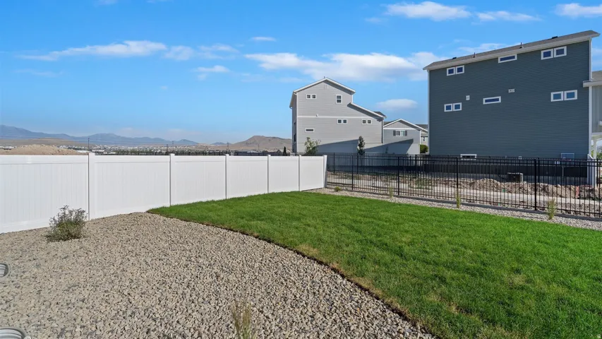 Expansive backyard with a manicured lawn, gravel landscaping, and a white privacy fence
