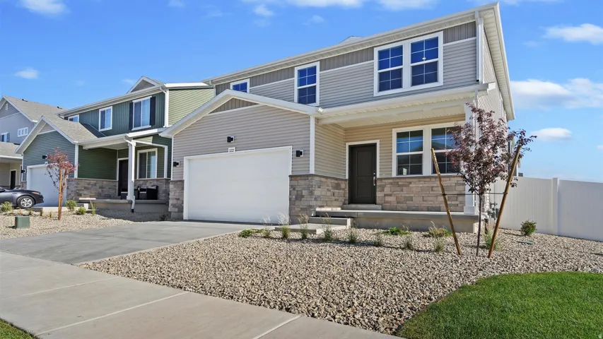 Contemporary two-story residence featuring a two-tone siding exterior, stone facade accents, an attached two-car garage, covered porch entry, and low-maintenance xeriscape landscaping