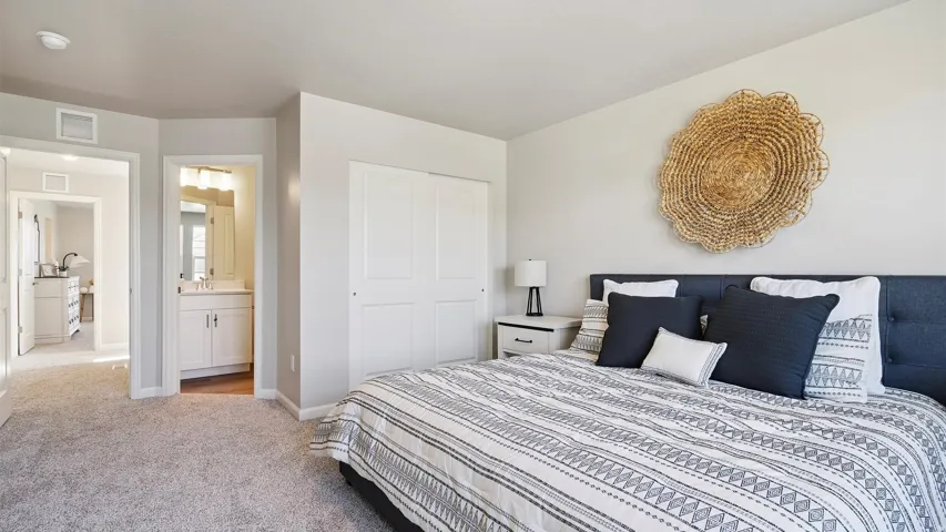 Carpeted bedroom featuring a closet with bi-fold doors, light gray wall paint, and an en-suite bathroom with a white vanity and mirror
