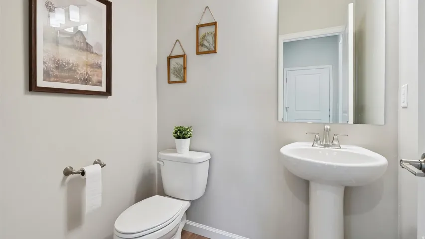 Bathroom featuring a pedestal sink with a chrome faucet, white toilet, and wood-finish flooring