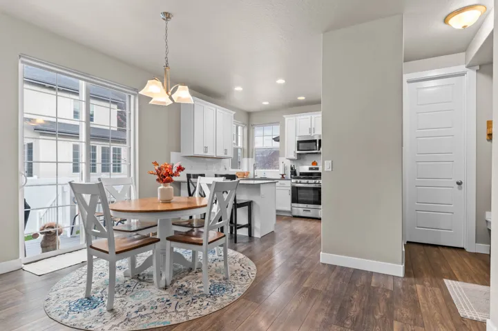 Open-concept dining and kitchen space featuring wood-finish flooring, white cabinetry, stainless steel appliances, and a tiled backsplash