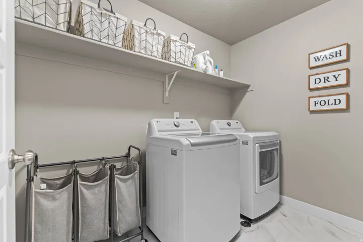 Dedicated laundry area featuring a wall-mounted shelving unit, contemporary appliances, and light-toned flooring