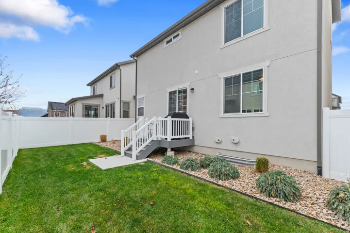 Fully fenced backyard featuring a manicured lawn, a raised deck with stairs, a gravel and shrub landscaping bed, and a stucco exterior