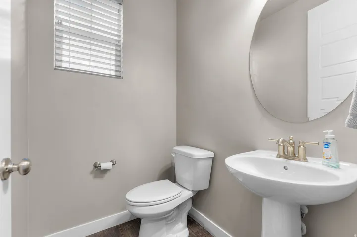 Pedestal sink with brushed brass-finish faucet, accompanied by a round wall mirror