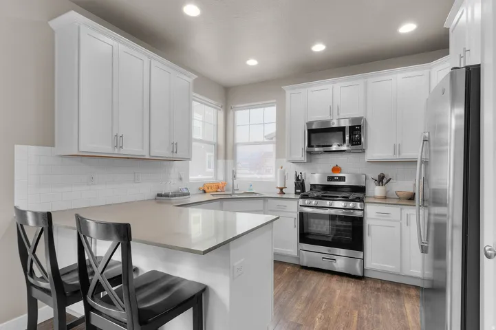 Kitchen featuring white shaker cabinetry, stainless steel appliances, a white subway tile backsplash, light-toned countertops, and wood-finish flooring