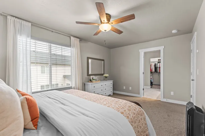 Carpeted primary bedroom with a window featuring blinds and sheer white curtains