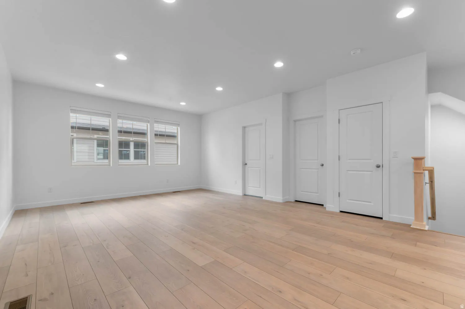 Spacious interior room featuring light wood-finish flooring, recessed lighting, and multiple windows with blinds