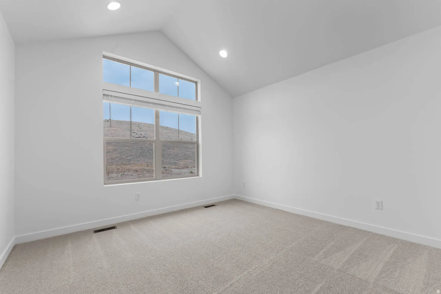 Vaulted ceiling room featuring a large window with transom, recessed lighting, and light-toned carpeting