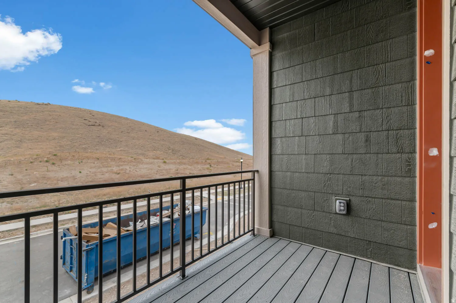 Balcony featuring composite decking, black metal railing, and a slatted green exterior wall