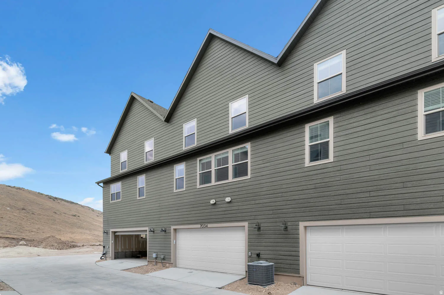 Multi-story property with horizontal siding, multiple windows, attached garages with white doors, and a clear concrete driveway