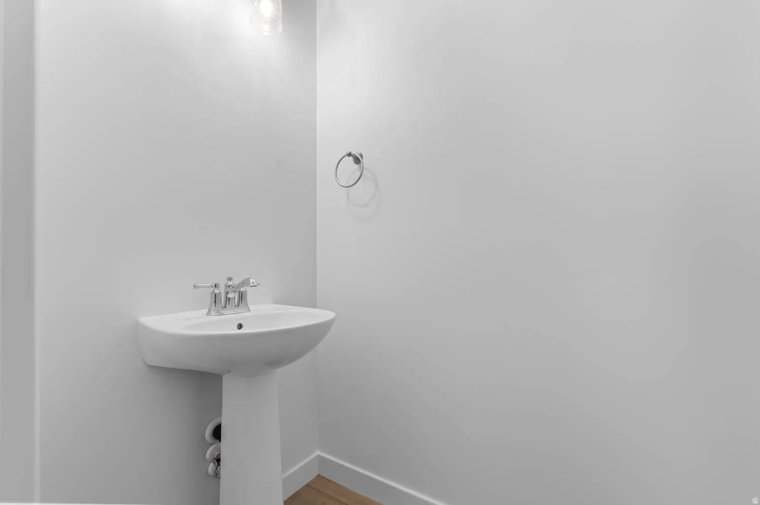 Pedestal sink with chrome faucet set, overhead vanity lighting, and wood-finish flooring