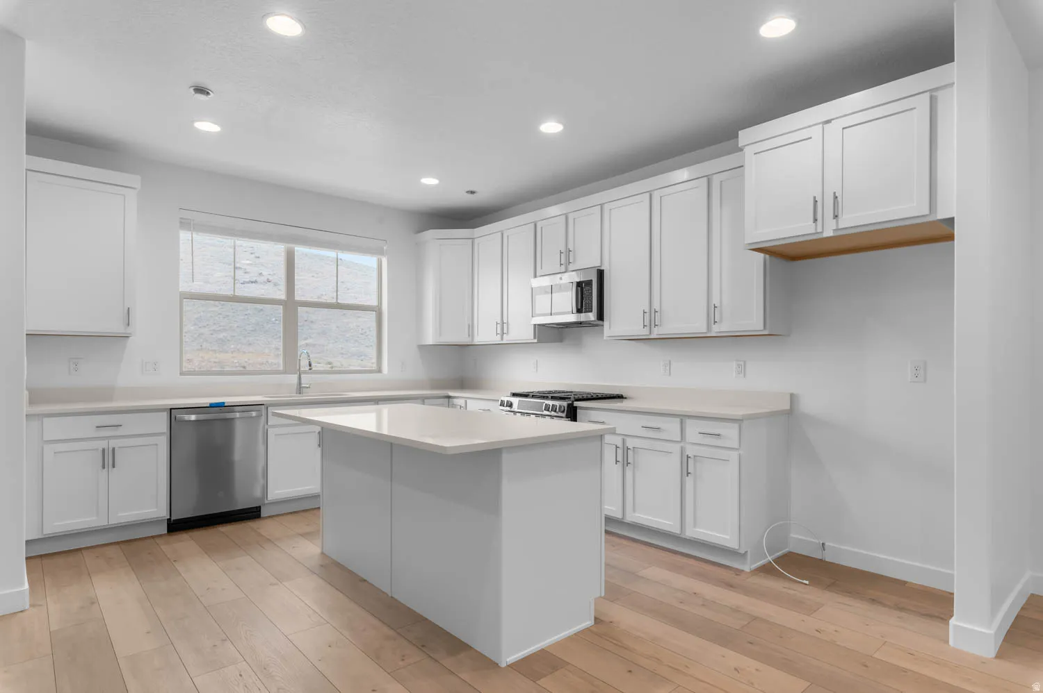 Kitchen featuring a central island, white shaker cabinetry, stainless steel appliances, light-toned countertops, and wood-finish flooring