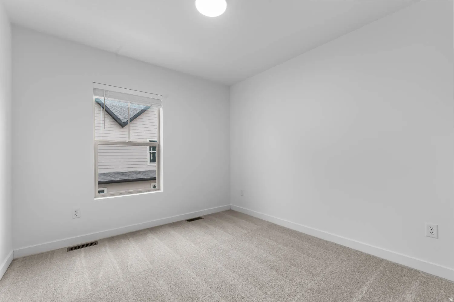 Light-filled interior space featuring neutral carpeting, white walls, and a recessed window with blinds