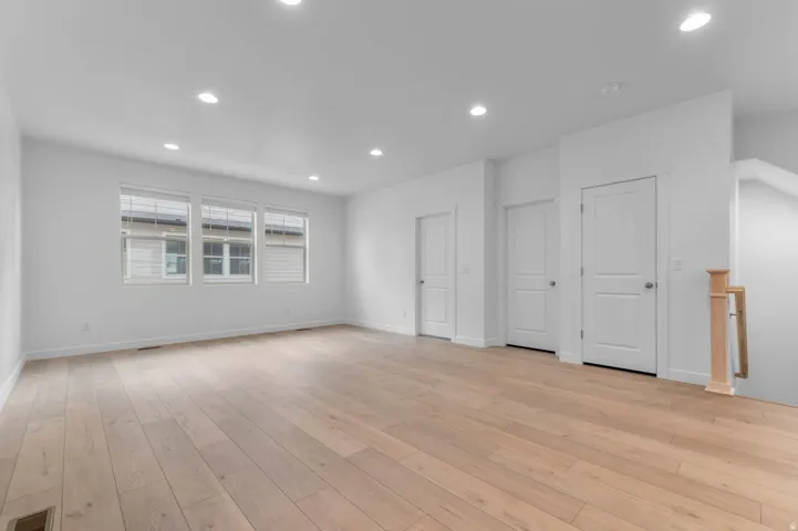 Spacious interior room featuring light wood-finish flooring, recessed lighting, and multiple windows with blinds