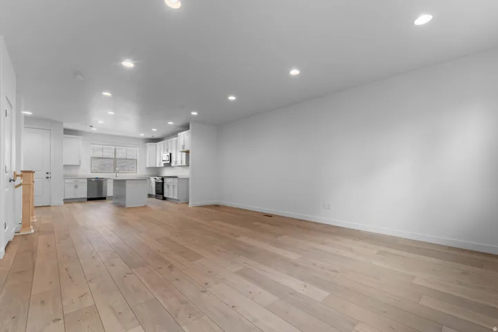 Open-concept interior featuring light wood-finish flooring, recessed lighting, and a white kitchen with an island, stainless steel appliances, and white cabinetry