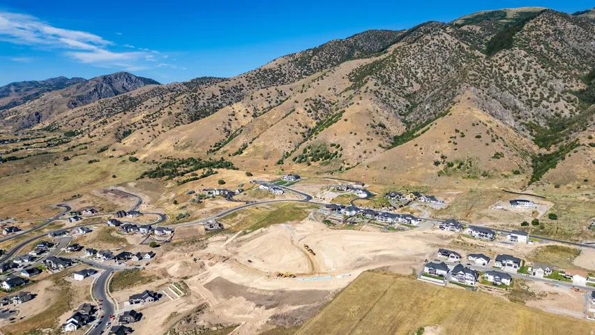 Aerial perspective showcasing a developing residential area with paved streets, scattered homes with dark roofs, and mountain terrain in the background