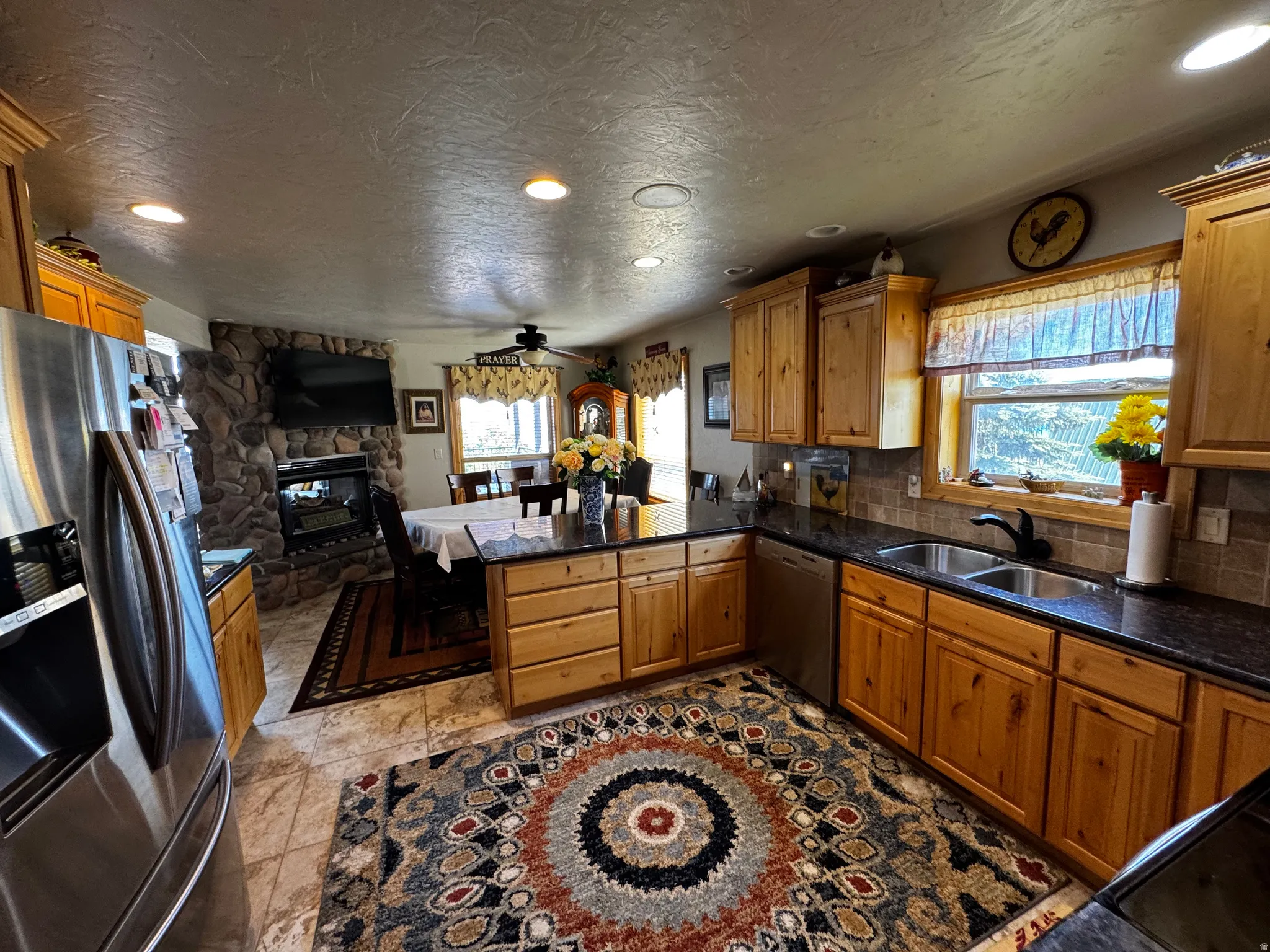 Open-concept kitchen featuring light wood cabinetry, dark countertops, a double basin sink, and tile flooring