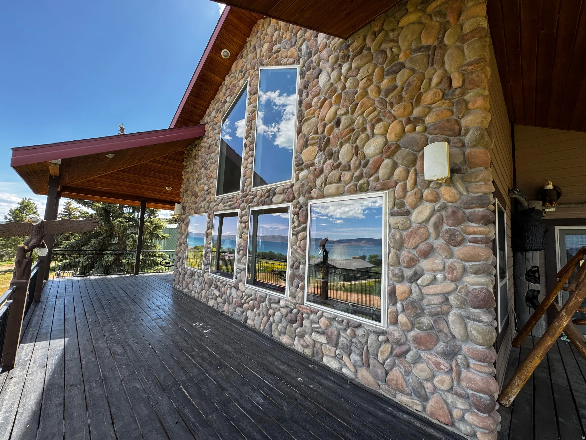Exterior stone facade with multiple windows, featuring an expansive wooden deck, wooden soffit, and exposed rafter tails