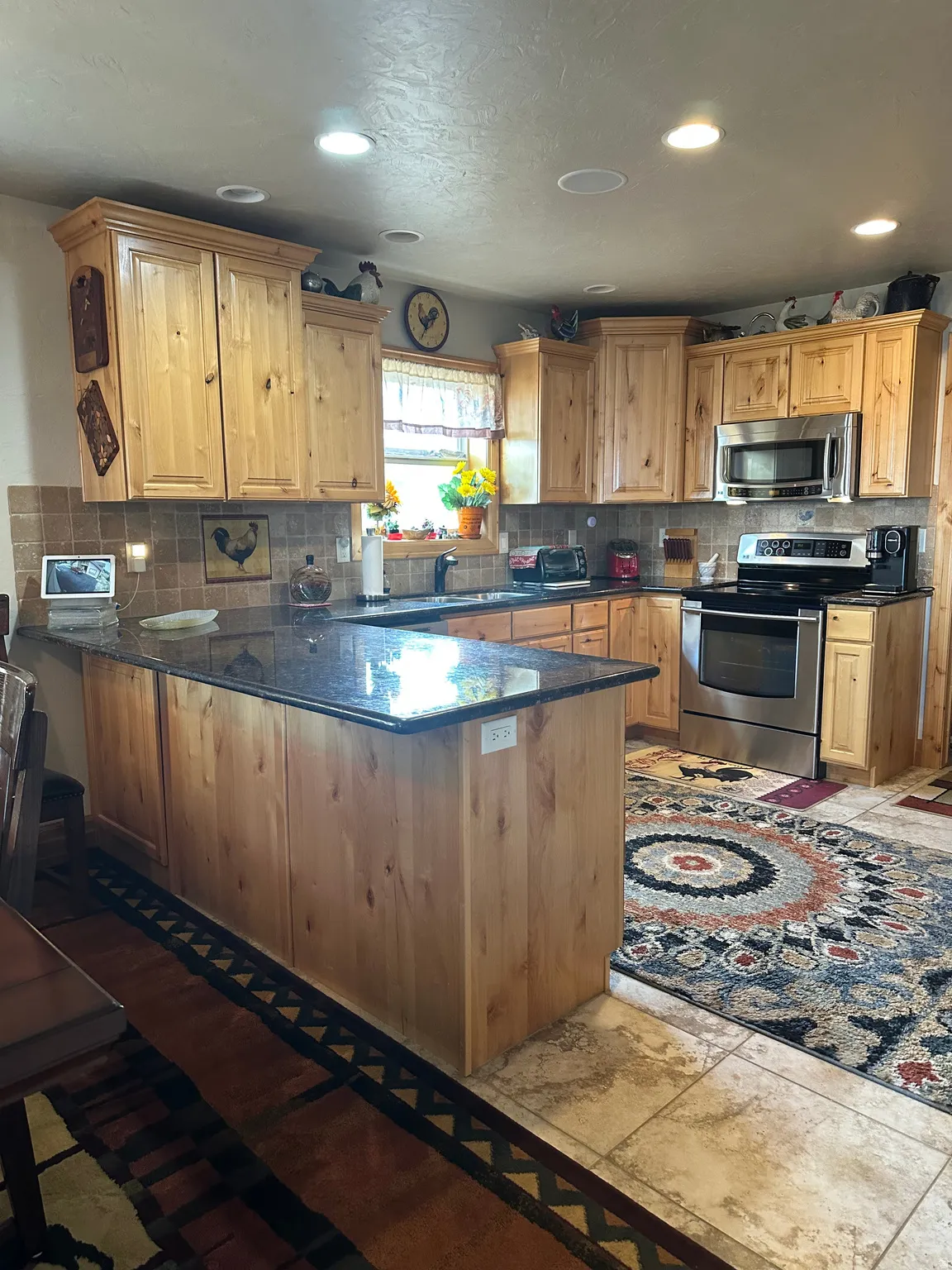 U-shaped kitchen featuring wood cabinetry, dark countertops, a tile backsplash, and stainless steel appliances