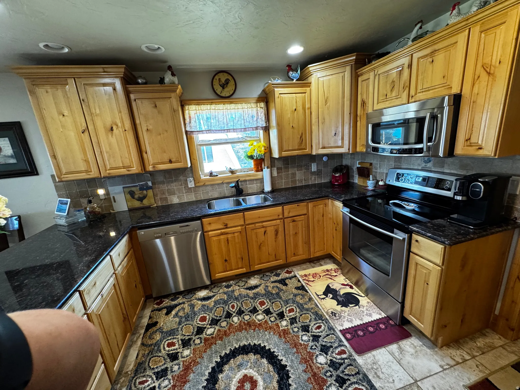 Kitchen featuring wood-finish cabinetry, dark countertops, a stainless steel dishwasher, and a stainless steel range with an overhead microwave