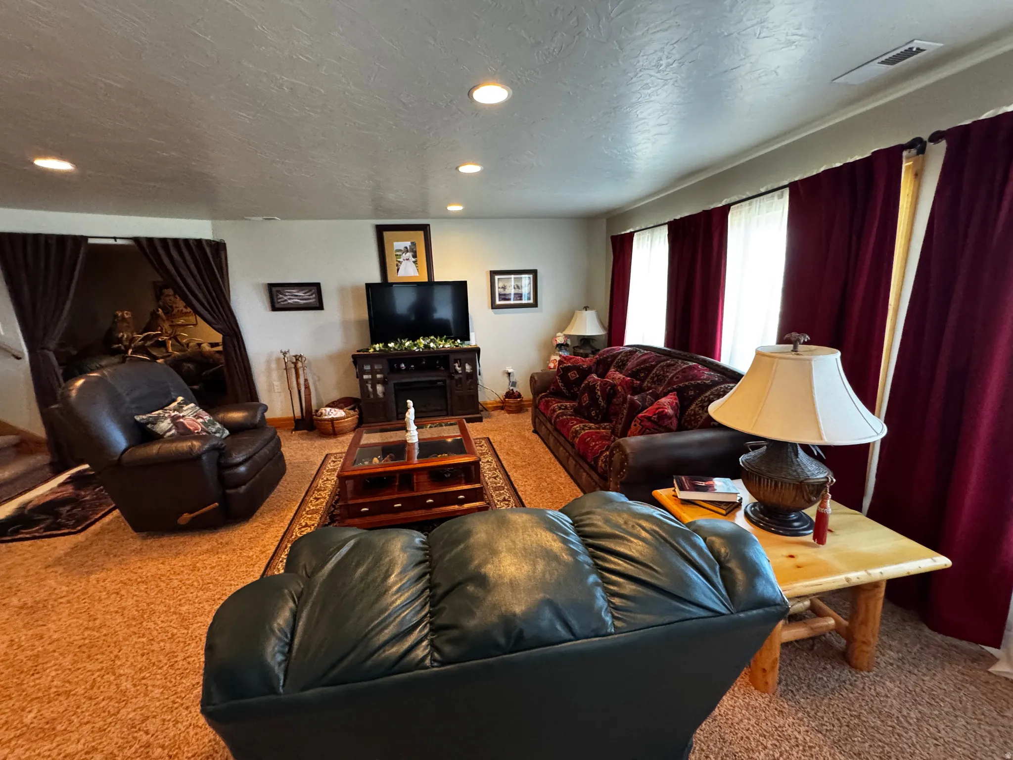 Carpeted living area featuring recessed ceiling lighting, a built-in media console with an electric fireplace, and multiple windows dressed with full-length drapery
