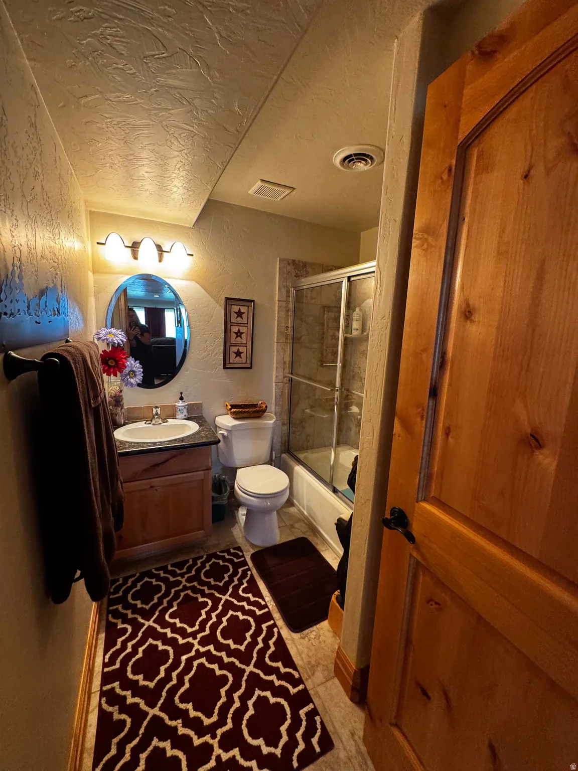 Full bathroom featuring a wood vanity with a solid surface countertop, a round mirror, and a shower-tub combination with a sliding glass door