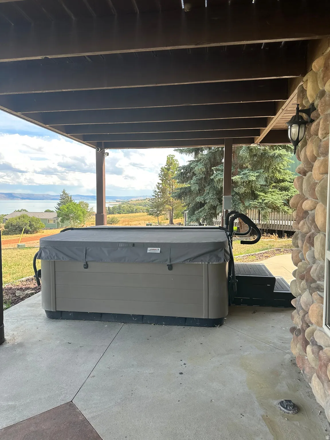 Covered patio with a spa, a stone-clad exterior wall, and a distant body of water