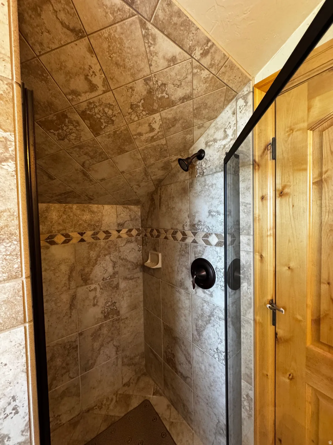 Tiled shower with a decorative mosaic accent band, oil-rubbed bronze fixtures, and a clear glass enclosure