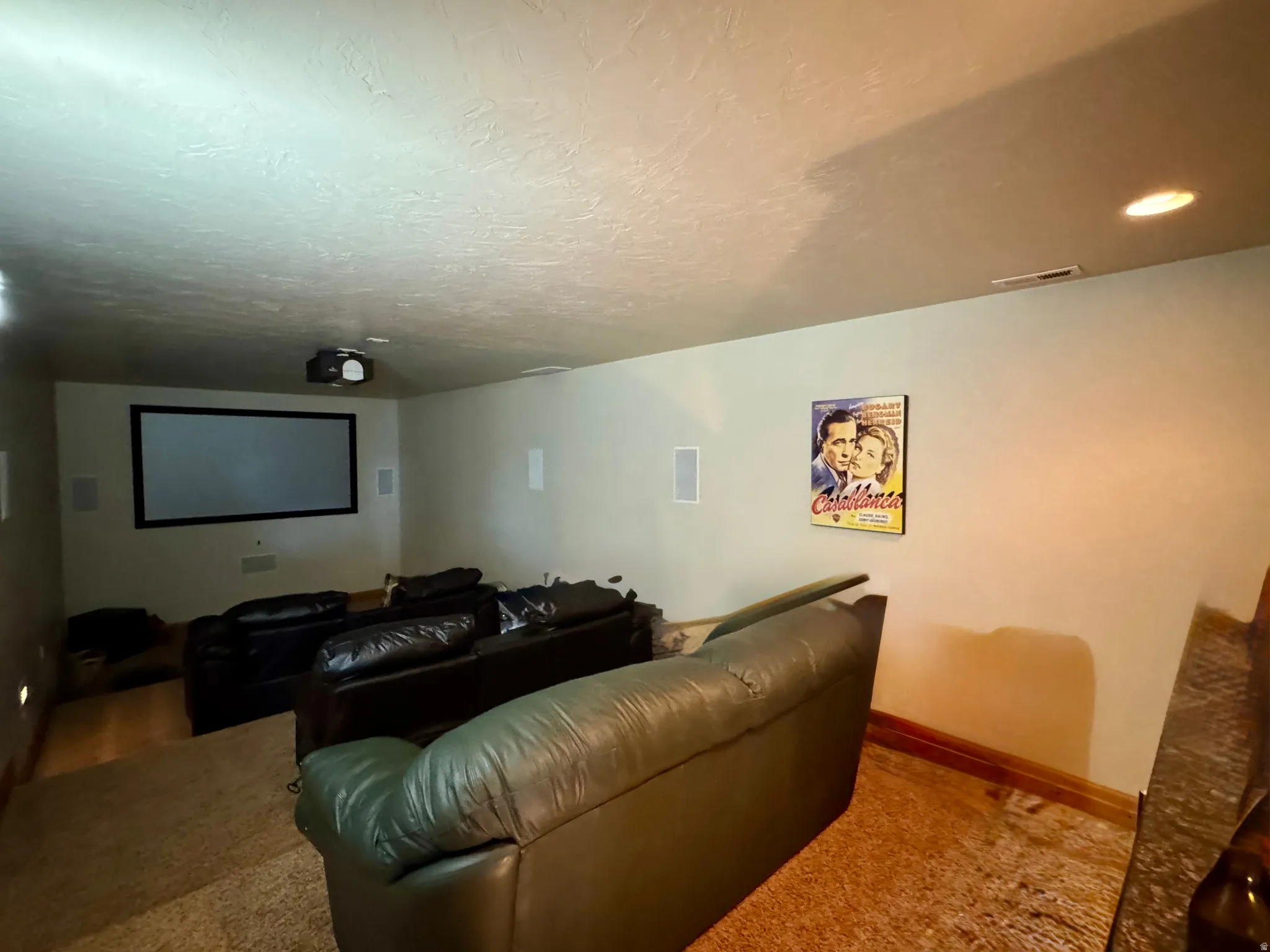 Dedicated media room featuring a mounted projector, large projection screen, recessed ceiling lighting, and built-in wall speakers